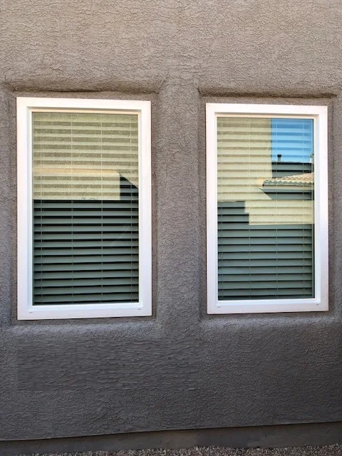 Two new white retrofit windows with shutters on a tan stucco wall