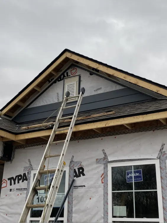 New white windows set in a house wrapped wall beside a ladder at the gable