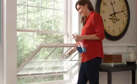 Woman cleaning the outside glass of a double hung window tilted into the room