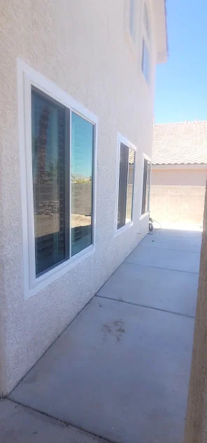Two white replacement windows set into a stucco wall beside a driveway path
